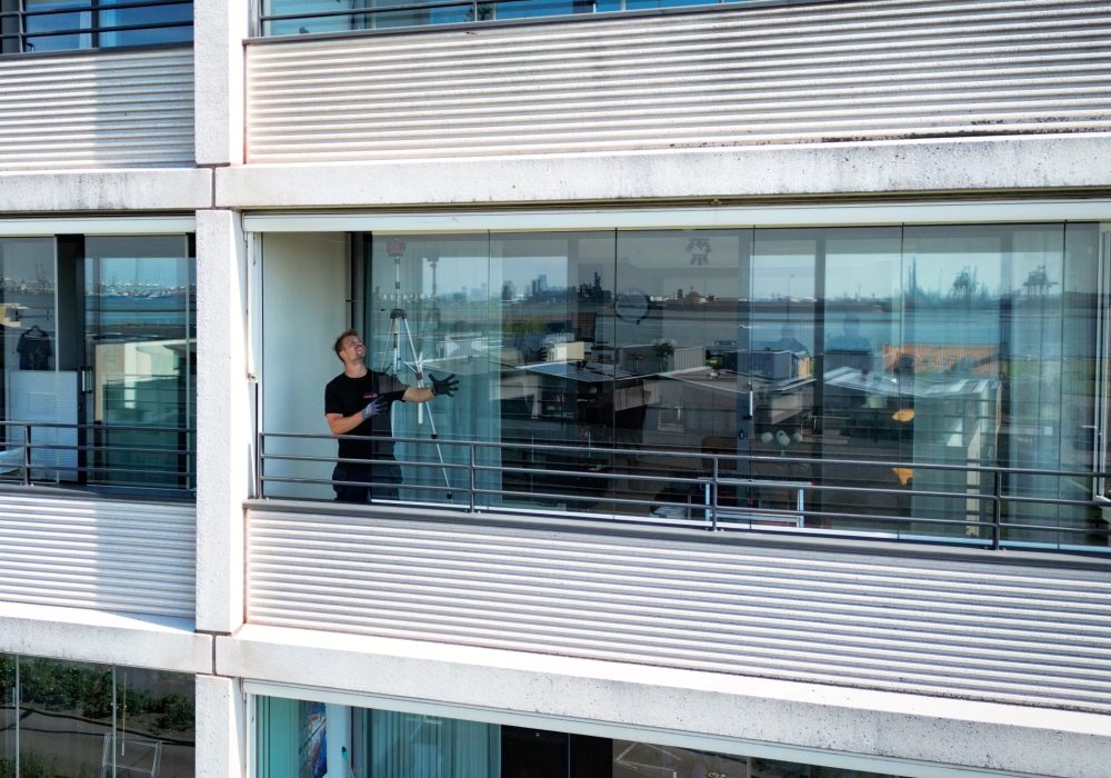 default Totaalbeeld van buitenuit waar man te zien is die de balkonbeglazing op de juiste plek zet