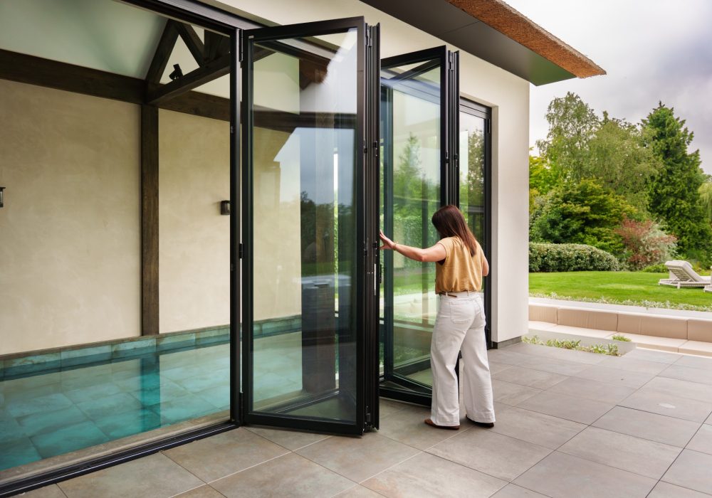 VMR-Vouwwanden-tuin-aanbouw 4 Buitenaanzicht van een luxe villa met grote glazen vouwwanden die uitkijken op het binnenzwembad