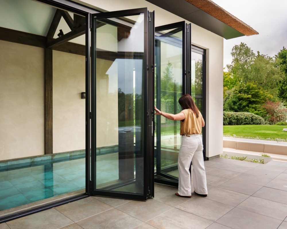 Buitenaanzicht van een luxe villa met grote glazen vouwwanden die uitkijken op het binnenzwembad